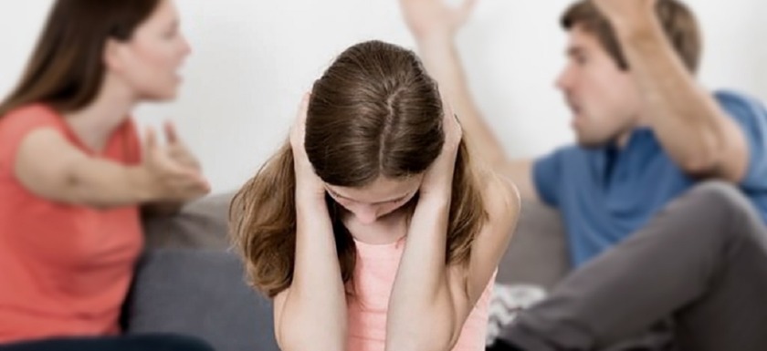 violencia doméstica: imagen en primer plano de una niña tapándose los oídos para no oír la discusión de sus padres detrás de ella