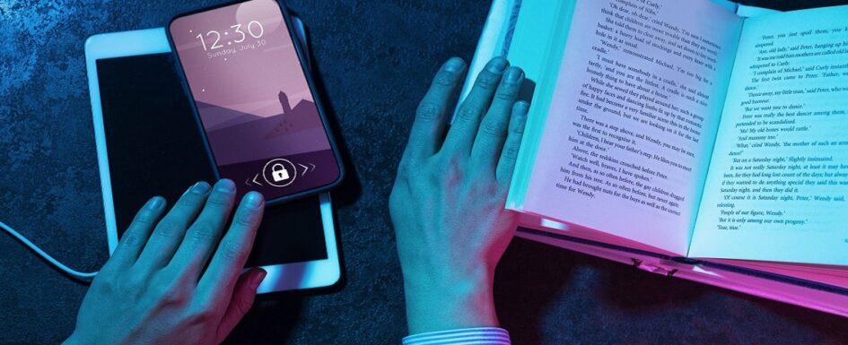Manos sosteniendo un libro abierto mientras interactúan con un smartphone y una tableta, explorando diversas apps de lectura accesible. La pantalla del smartphone muestra la hora y la fecha con un bloqueo activo. Iluminación en tonos azul y rosa que crea un contraste visual atractivo.