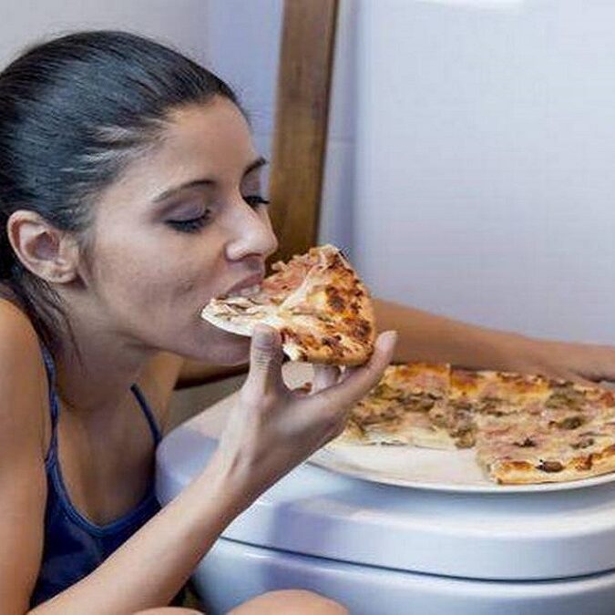 imagen de una joven comiendo en el cuarto de baño preparándose para vomitar lo comido.